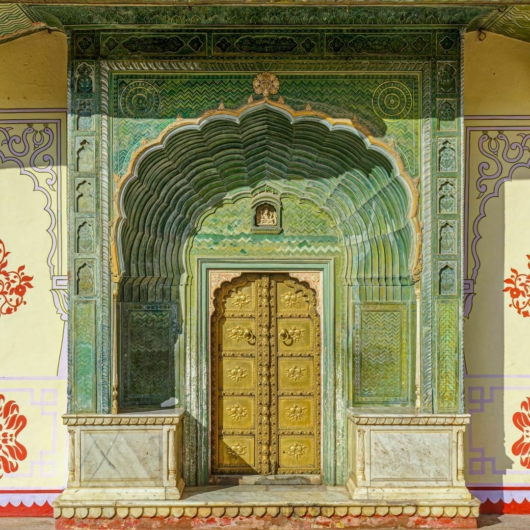 Auto-generated description: A beautifully ornate, green-arched doorway with intricate carvings and a golden door, surrounded by colorful decorative patterns.