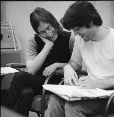 Late-Beatles era John Lennon and Paul McCartney are sitting together, smiling and looking at documents.